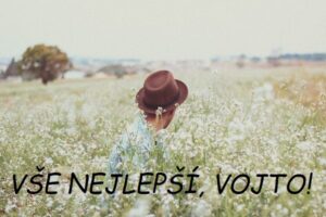 Muž, sedící zády k pozorovateli, na louce plné rozkvetlého lučního kvítí.