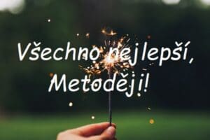 Nápis "Všechno nejlepší, Metoději!" na pozadí ruky, držící hořící prskavku v přírodě.